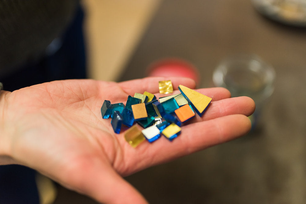 My hand holding luminous pieces of gold leaf smalti glass from Venice, materials that bring depth and richness to each mosaic.