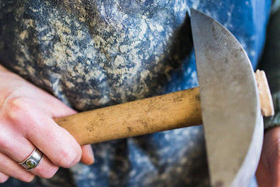 My hands holding a mosaic hammer and hardie, the traditional tools I use to shape each piece by hand.