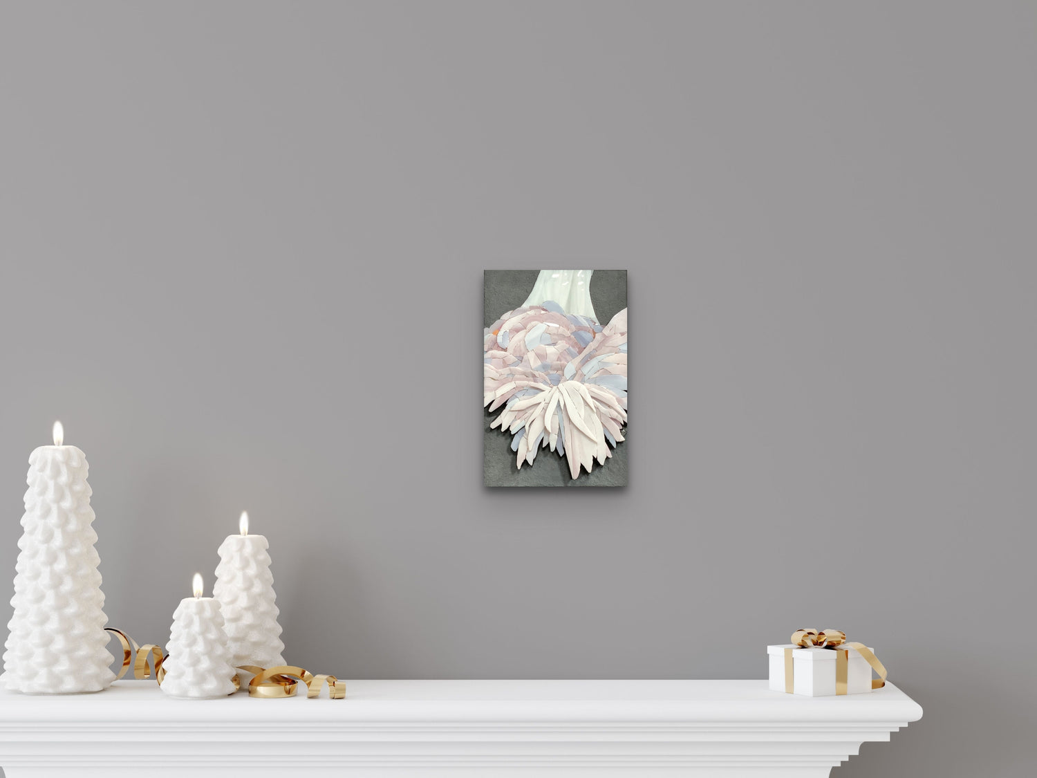 A soft-toned mosaic artwork by Maartje de Boer hanging above a white mantel, styled with sculptural white candles and soft lighting, evoking warmth, presence, and intelligent love.