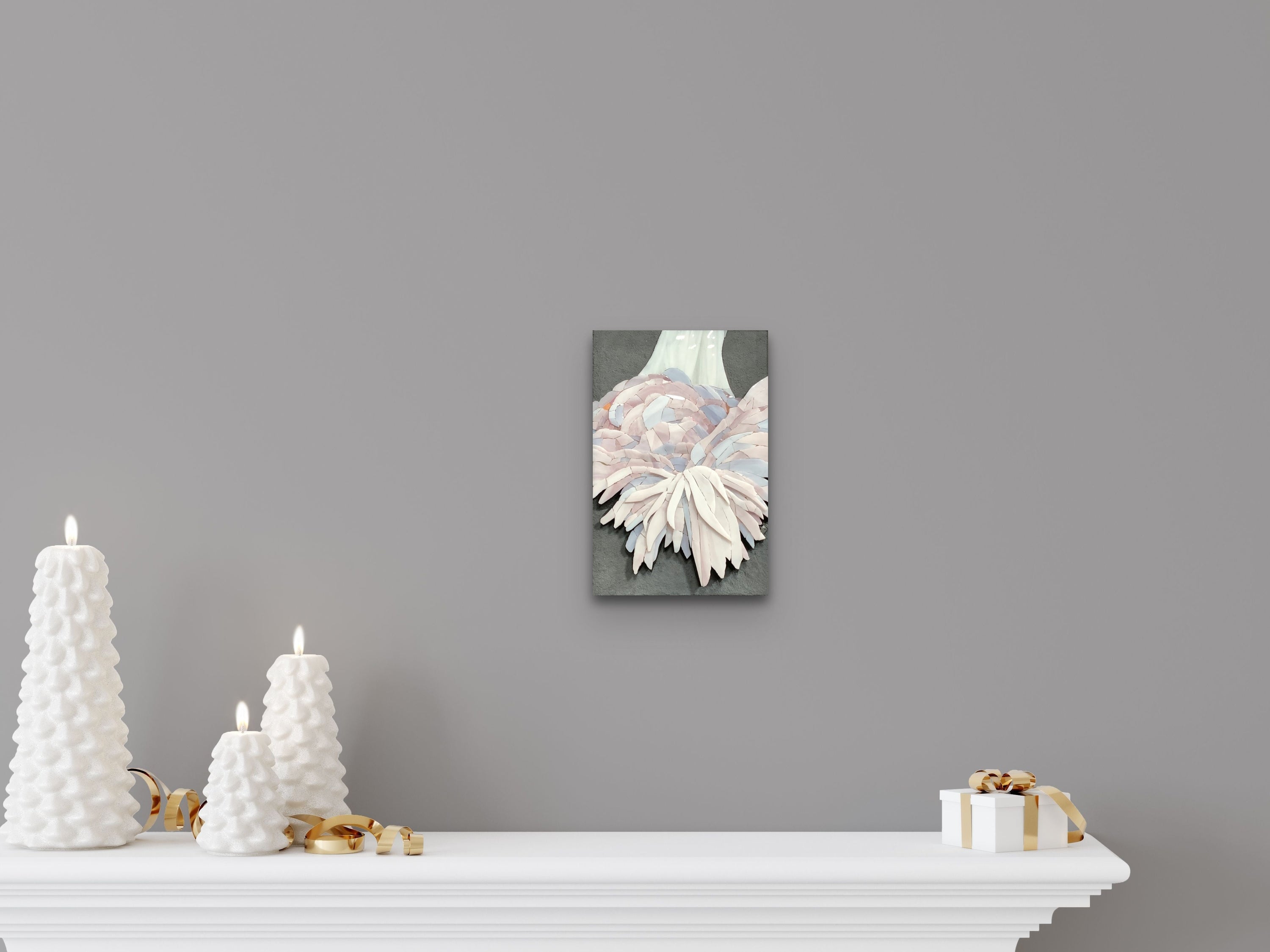 A soft-toned mosaic artwork by Maartje de Boer hanging above a white mantel, styled with sculptural white candles and soft lighting, evoking warmth, presence, and intelligent love.
