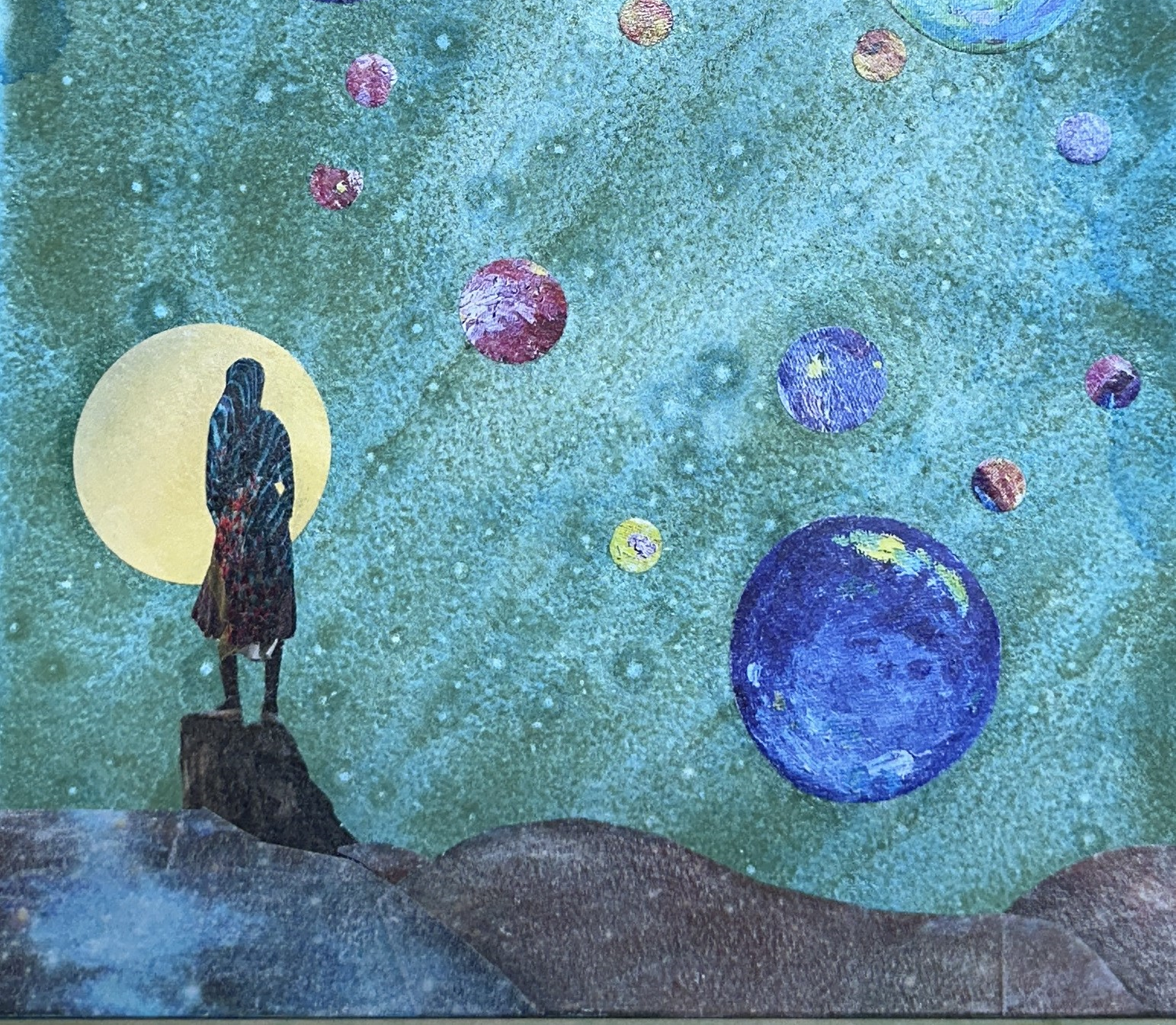 A hand-cut collage called 'She Will' of a woman standing on a hill beneath a sky filled with planets and moons, a visual reflection on the meaning of life and the quiet wonder of existing.