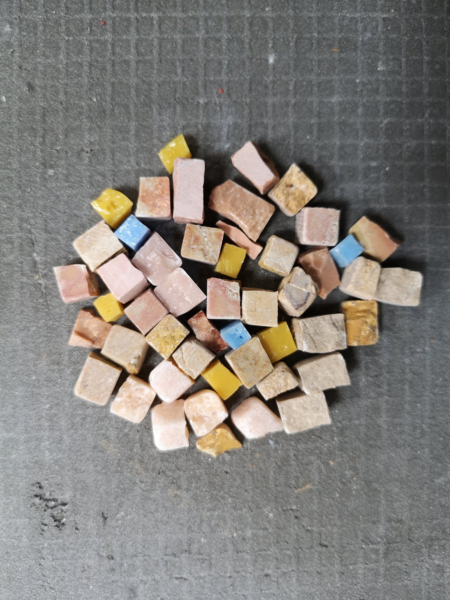 A cluster of colorful handmade mosaic tiles on a textured grey surface, a quiet composition full of creative potential and pause.