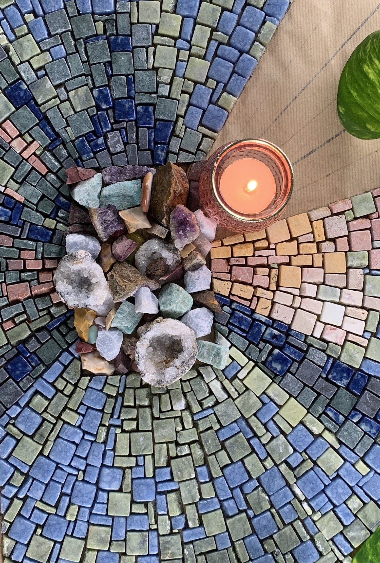 Top-down view of a candle and crystals placed at the center of a circular, blue-toned mosaic pattern. This photo reflects a calming, meditative space connected to the theme of creative flow.